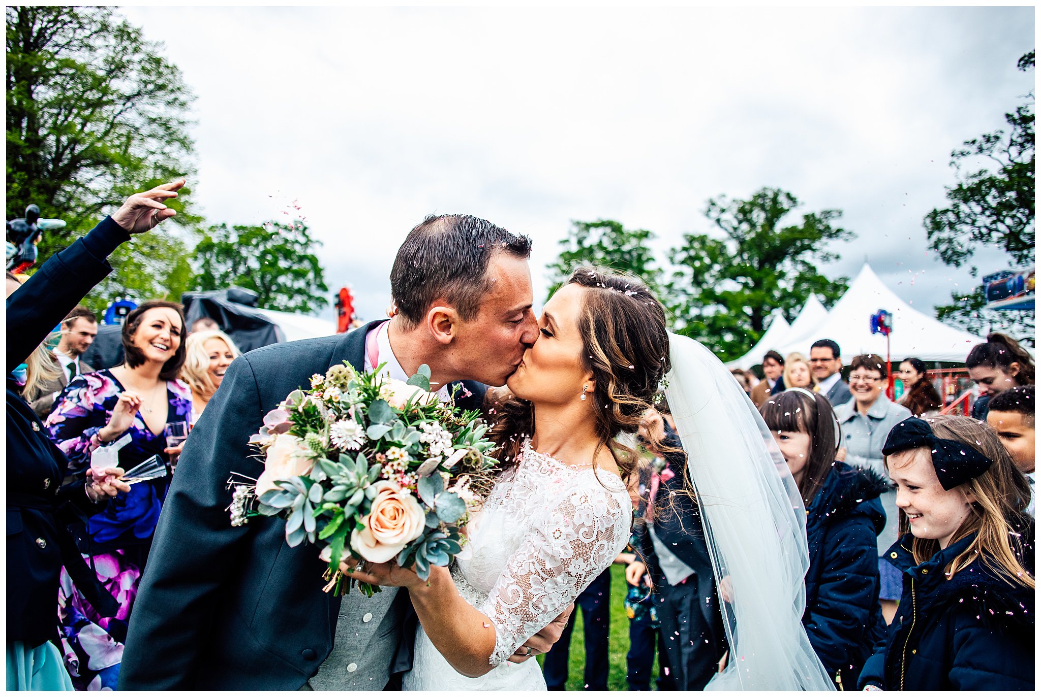 bride and groom kissing surrounded by people throwing confetti over them