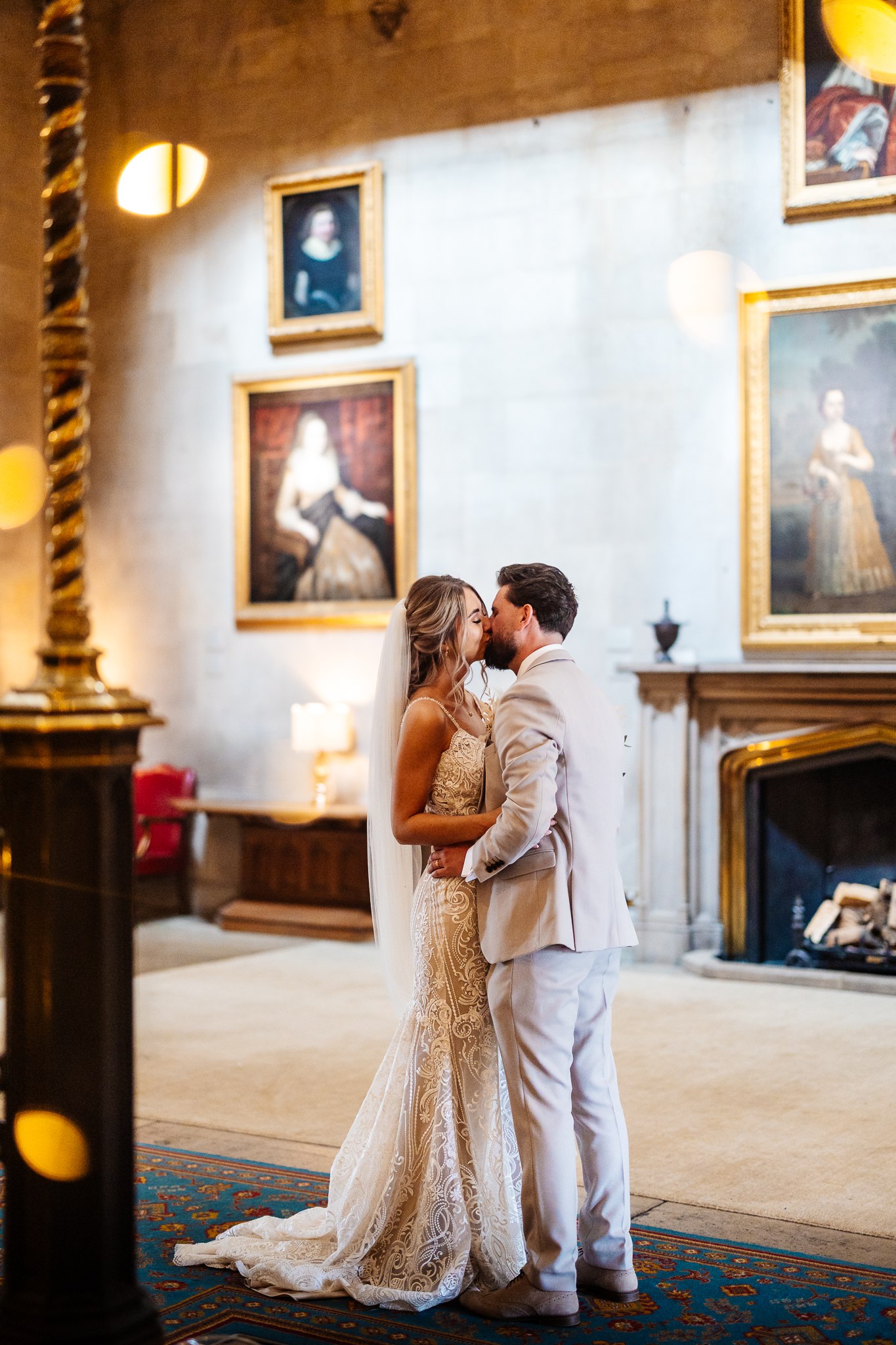 bride and groom kissing in front of paintings at ashridge house with lights surrounding them