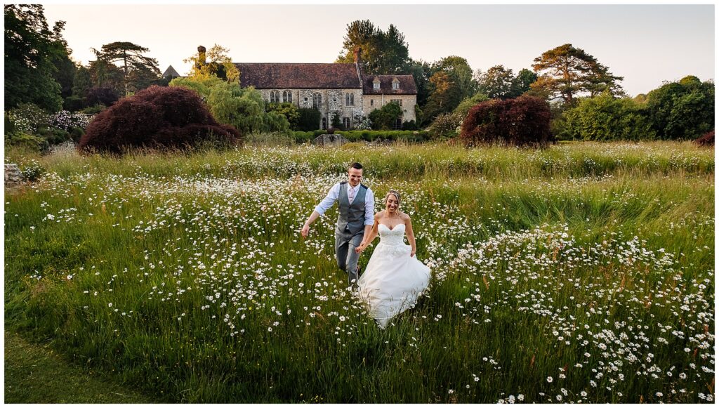 bride and groom walking through long wild flowers at nettlestead place