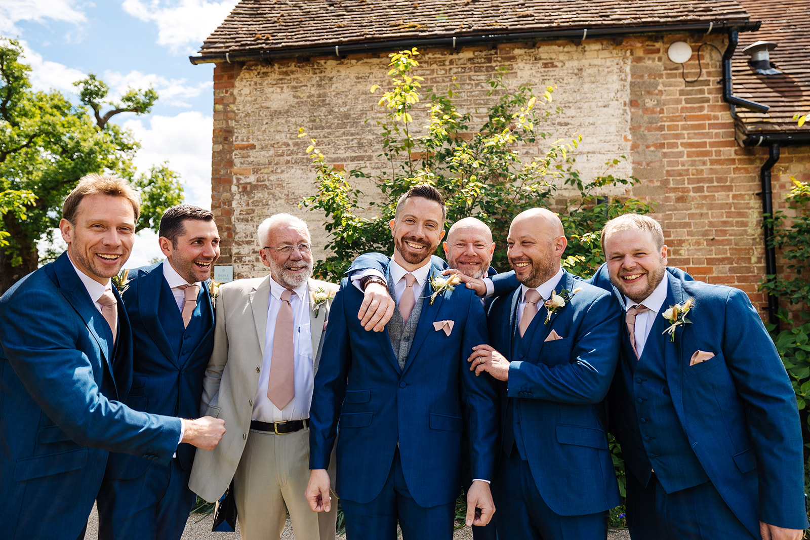 Groom with groomsmen, in dark blue suits with pink ties and pocket squares, outside Bassmead 