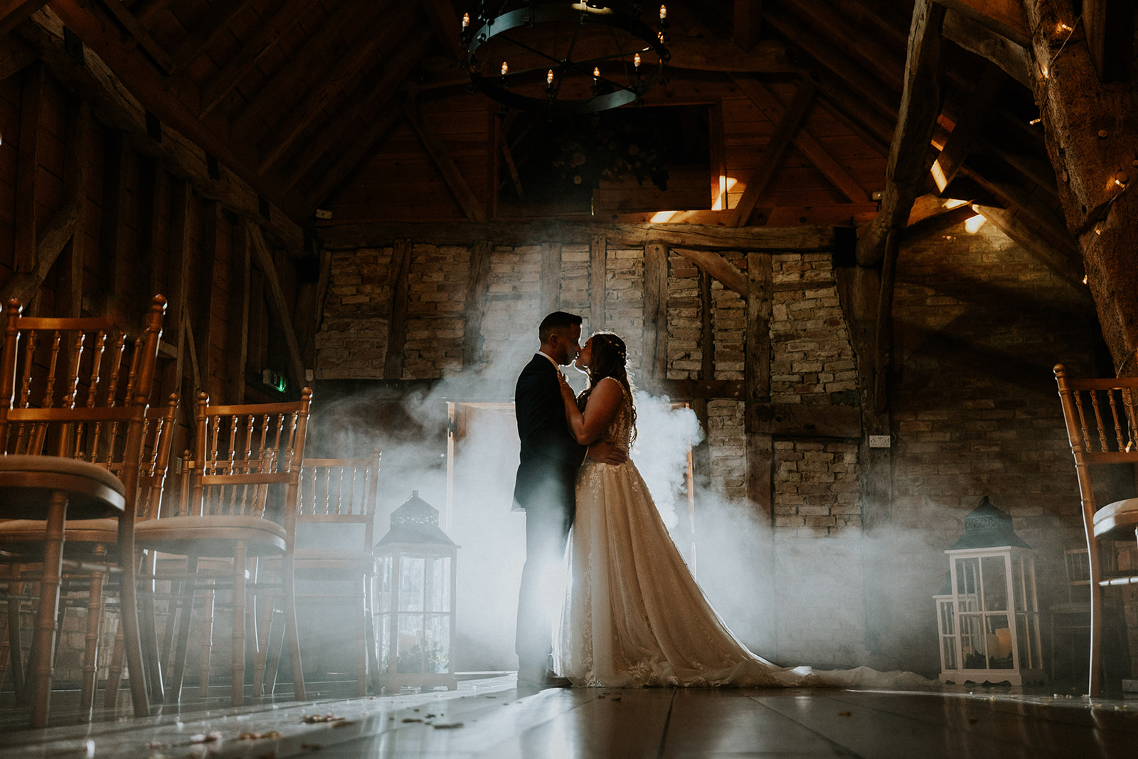 Couple share kiss in the barn, mist and exposed bricks and beams in the background