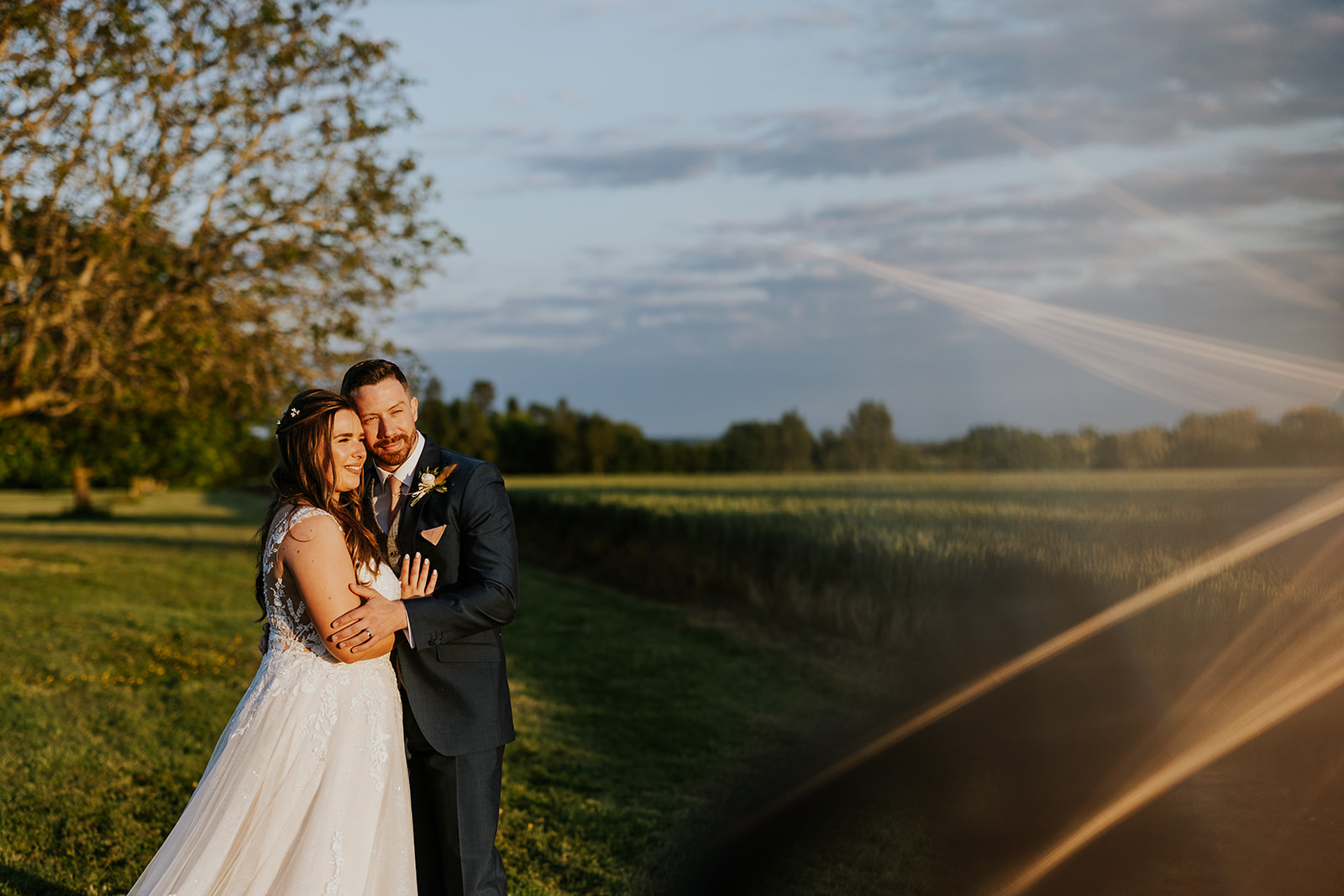 Couple watch the sun set over the fields by Bassmead