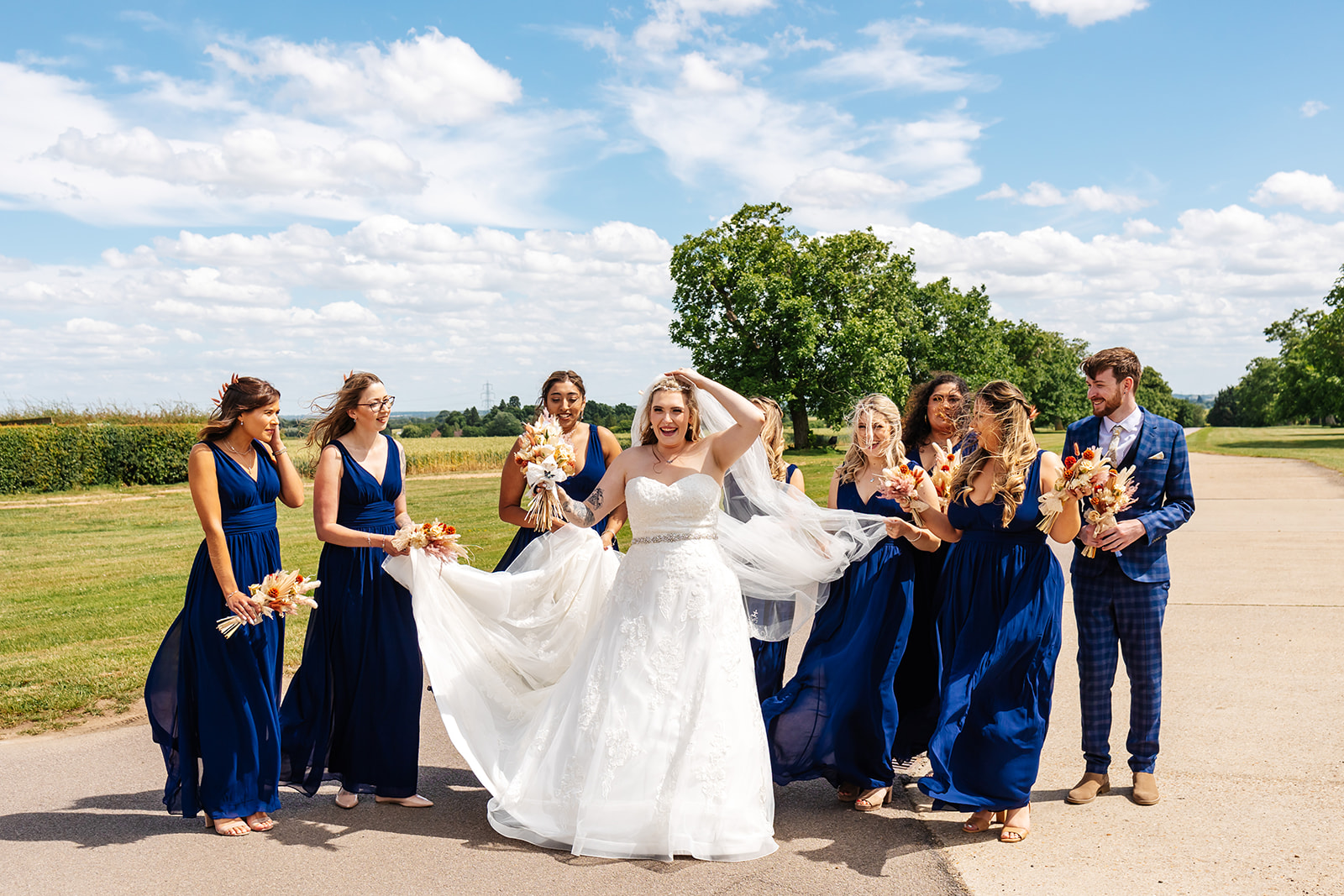 Bride and bridesmaids outside, walking, bride's veil is being held by bridesmaid