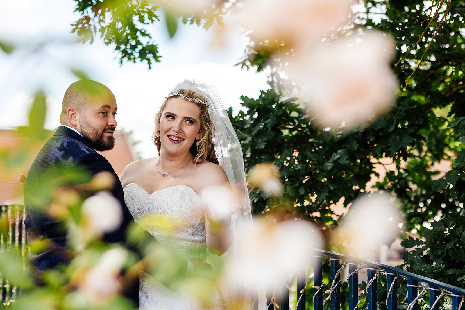 Couple stop on bridge at Bassmead, surrounded by greenery and flowers