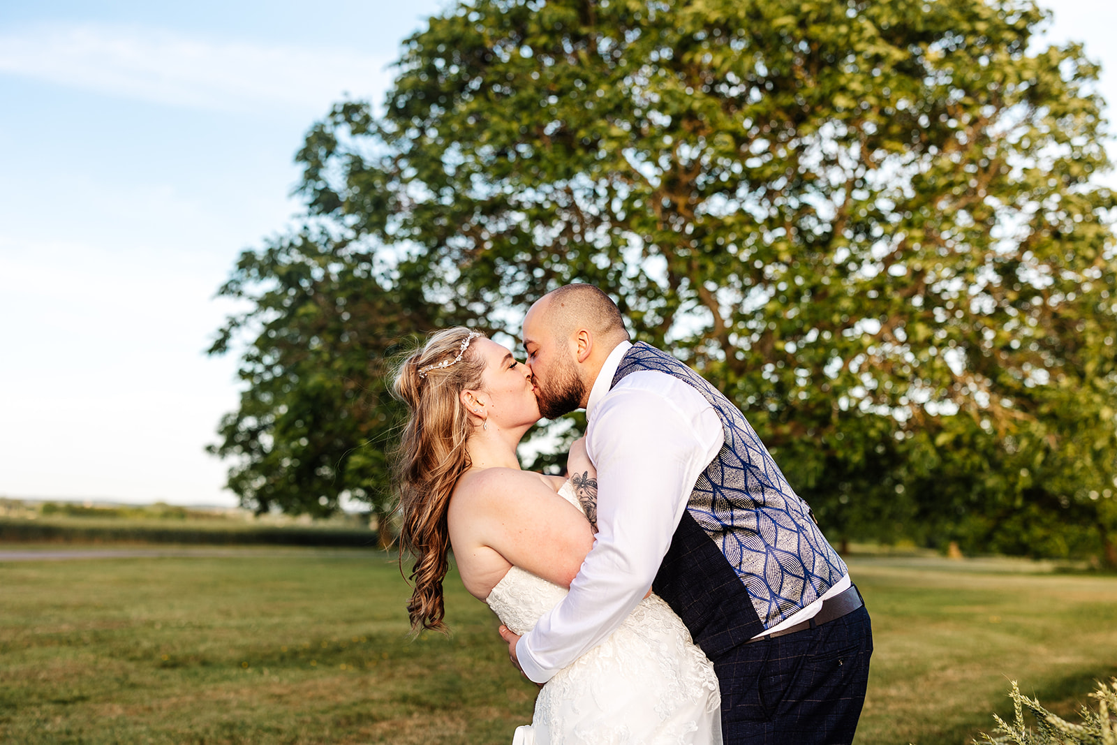 Couple share kiss outside with trees in the background. Bride is dipped by groom 