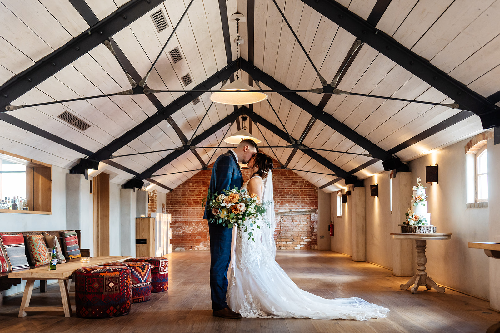 Bride & Groom post ceremony kissing inside venue with cake in the background