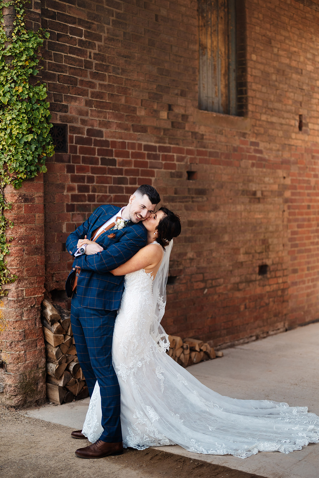 Bride hugging groom with her erms around his waist and kissing him on the cheek