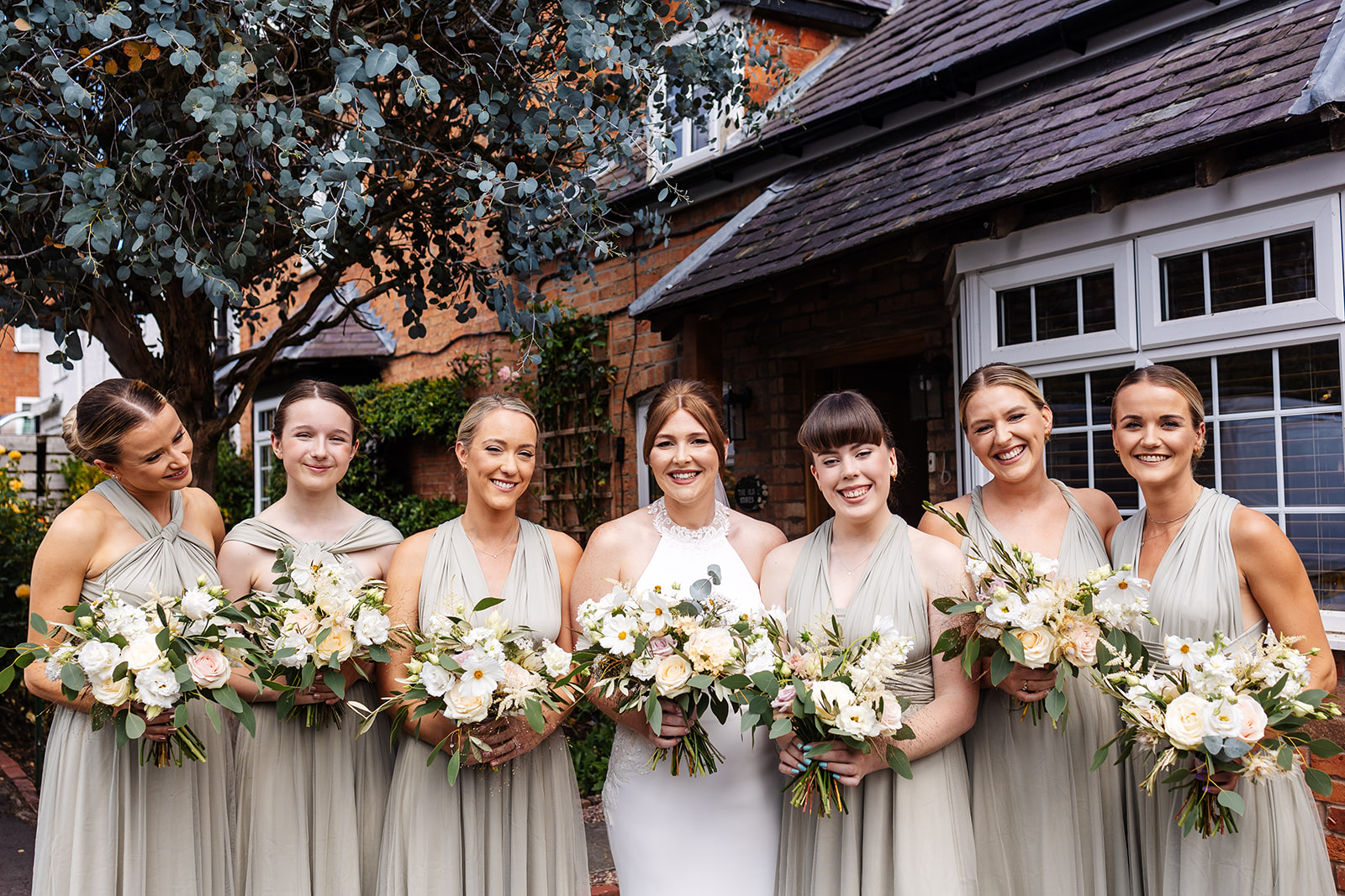 Bride and bridesmaids (in sage green dresses), they are al holding bouquets of pastel flowers 