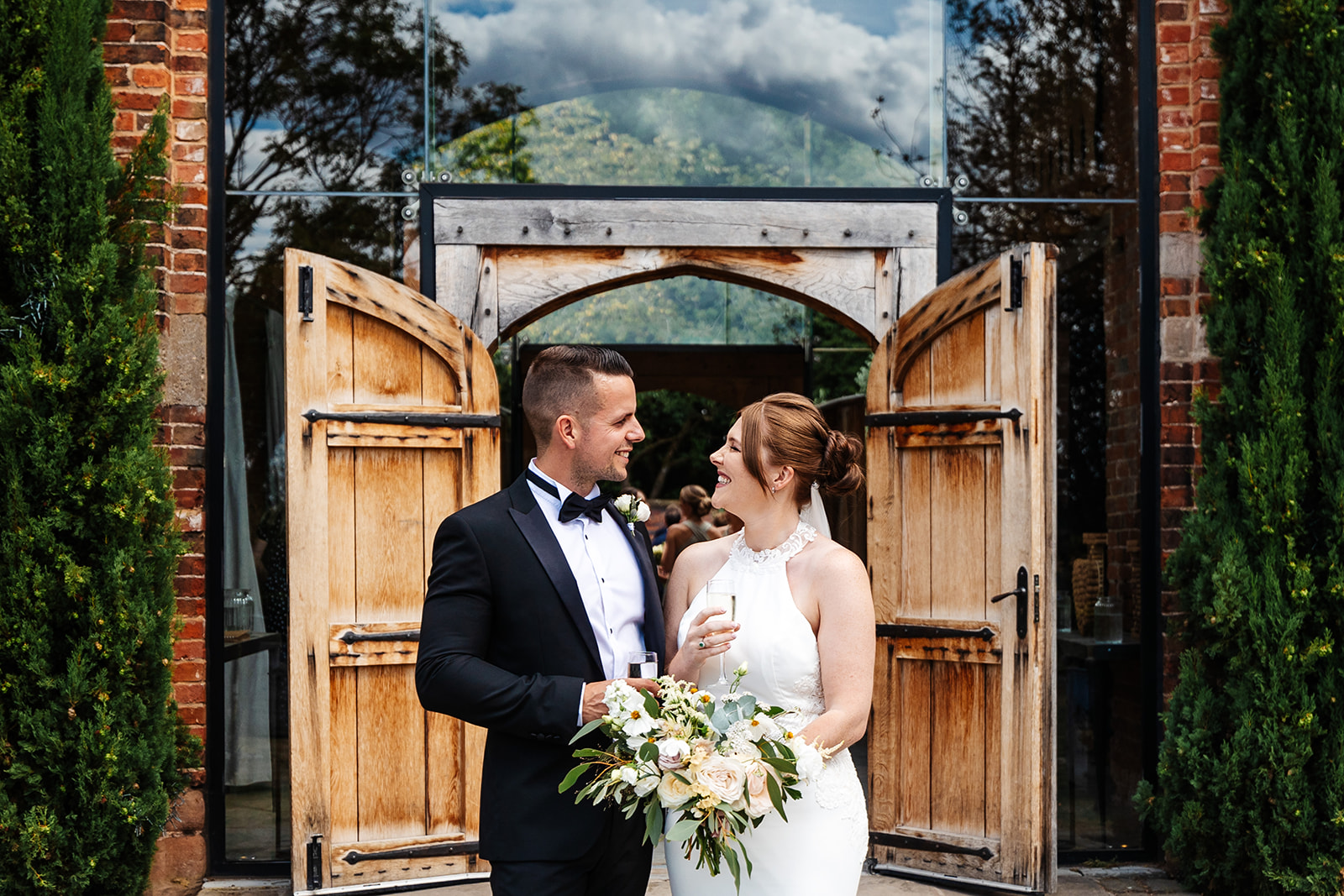 Couple outside ceremony space smiling at each other with a glass of bubbles in hand 