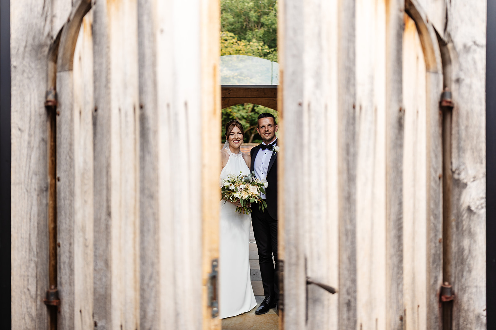 Couple peek through big wooden doors outside 