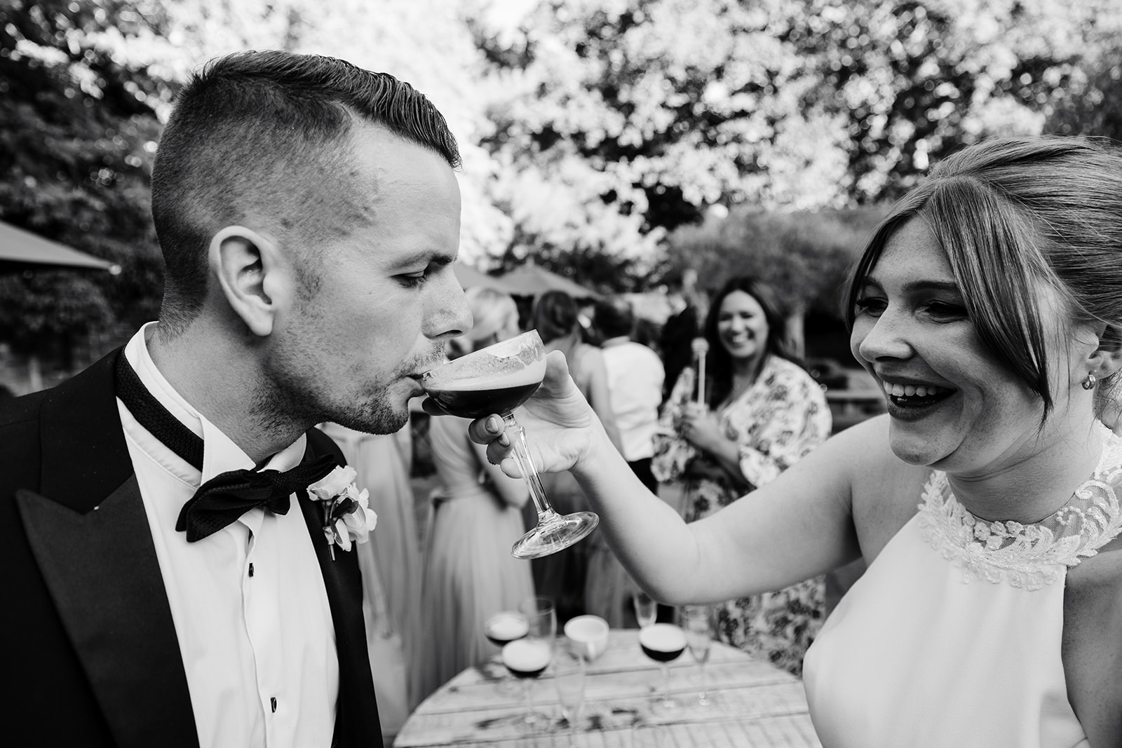 Groom takes sip of cocktail from bride, in black and white 