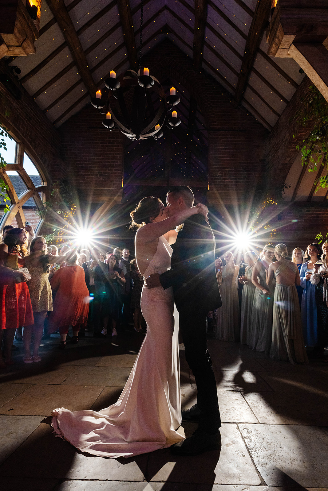 Couple share a kiss during first dance, spotlights shine in the background 