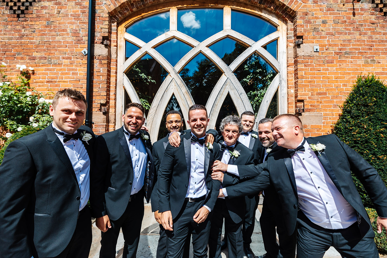 Groomsmen outside Shustoke Bar all in dark suits with bowties, the sun is shining 