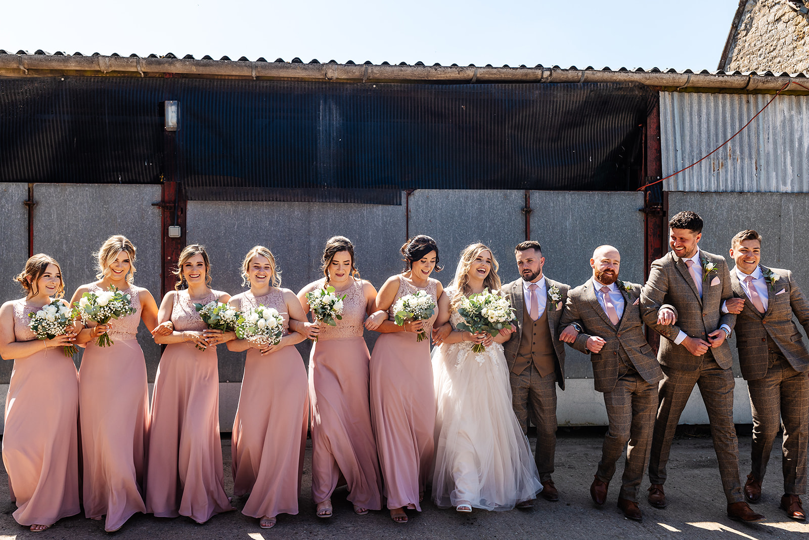 Couple with bridesmaids and groomsmen walking in a line outside barn 