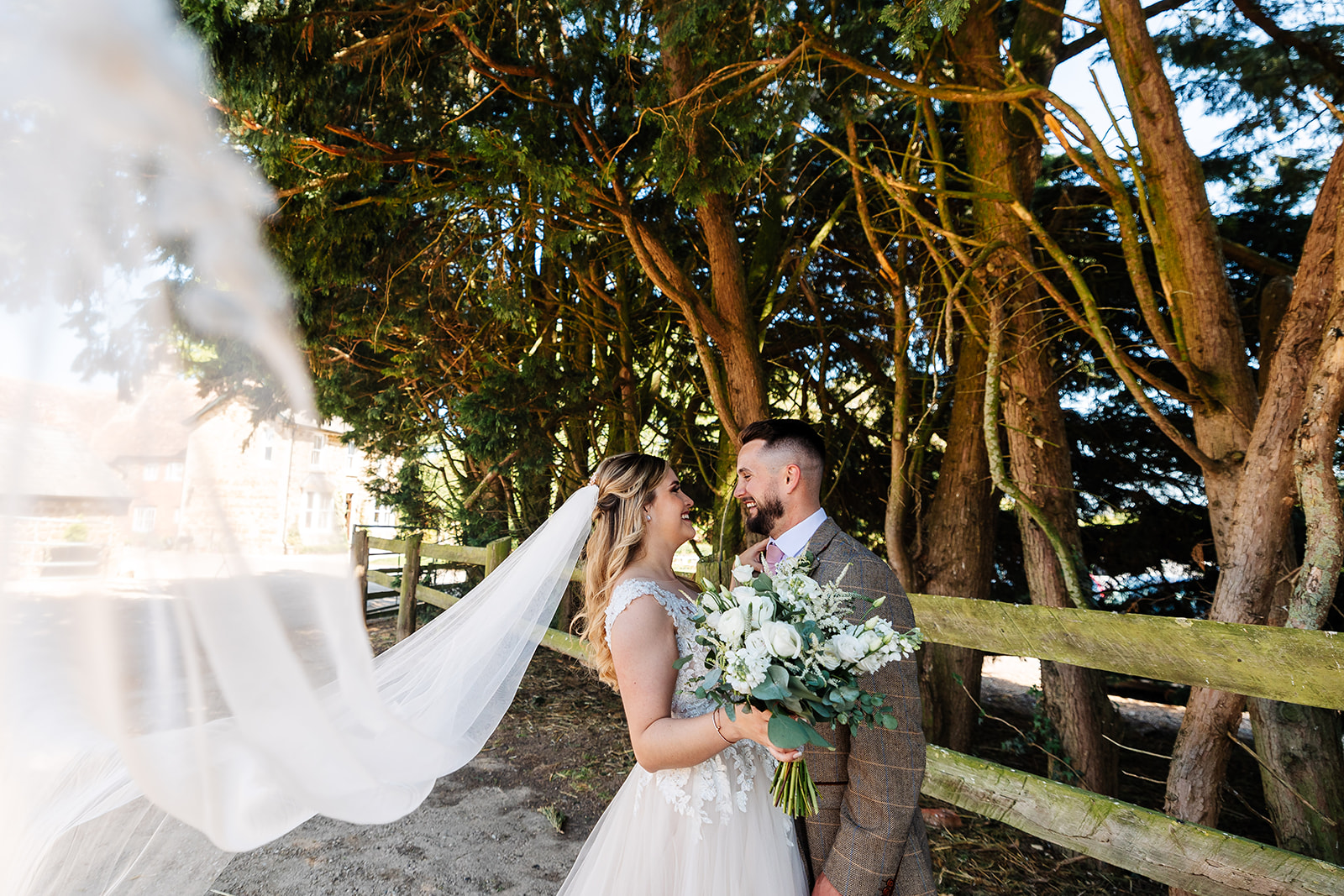 Couple share gaze Infront of forest area with brides veil blowing in the win