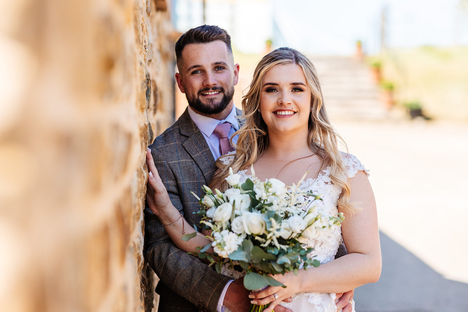 Couple shot outside leaning against sandstone brick wall 