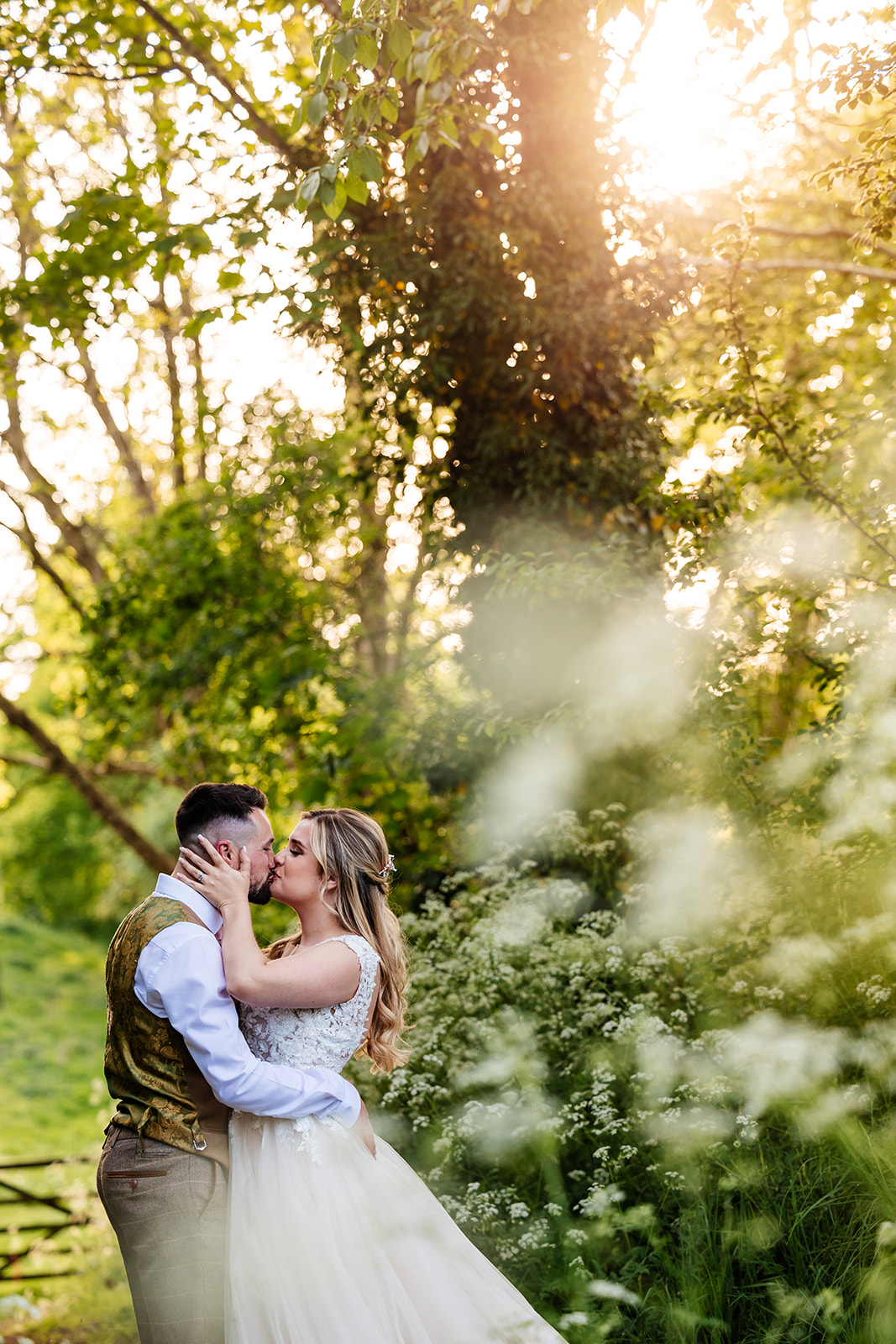 Couple share kiss in forest with white flowers and trees in the background 