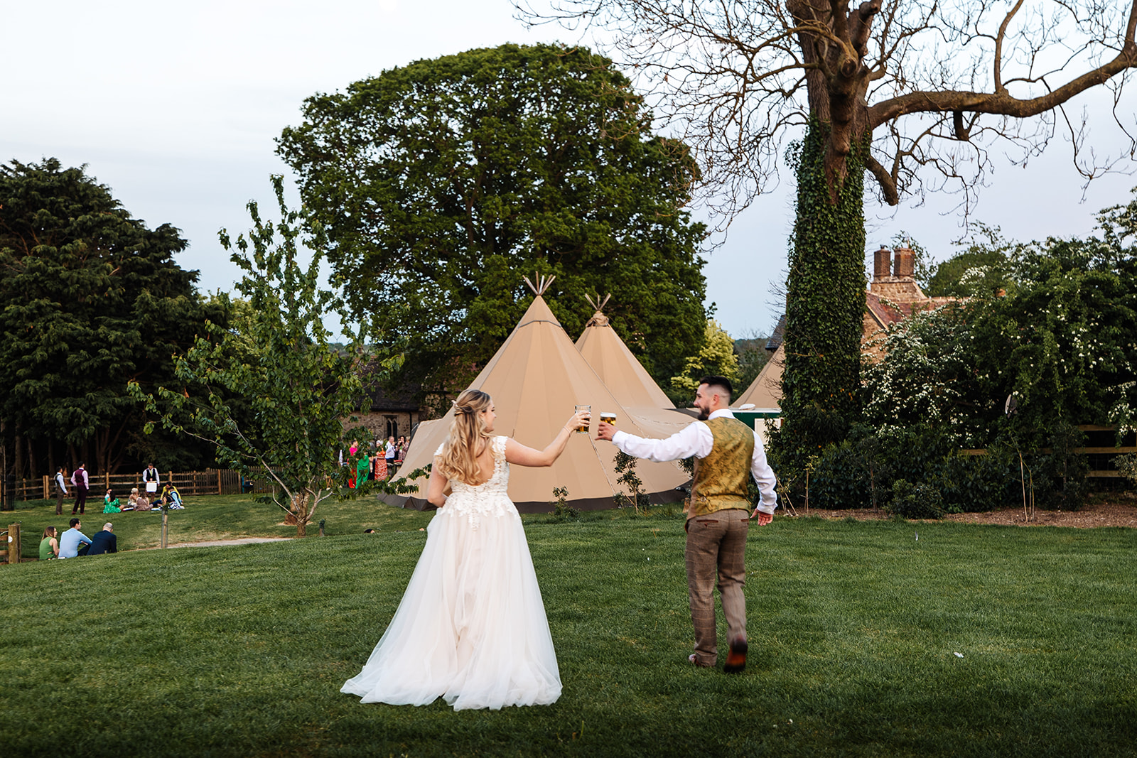 bride and groom cheers a beers walking towards tipi at dusk at slapton manor