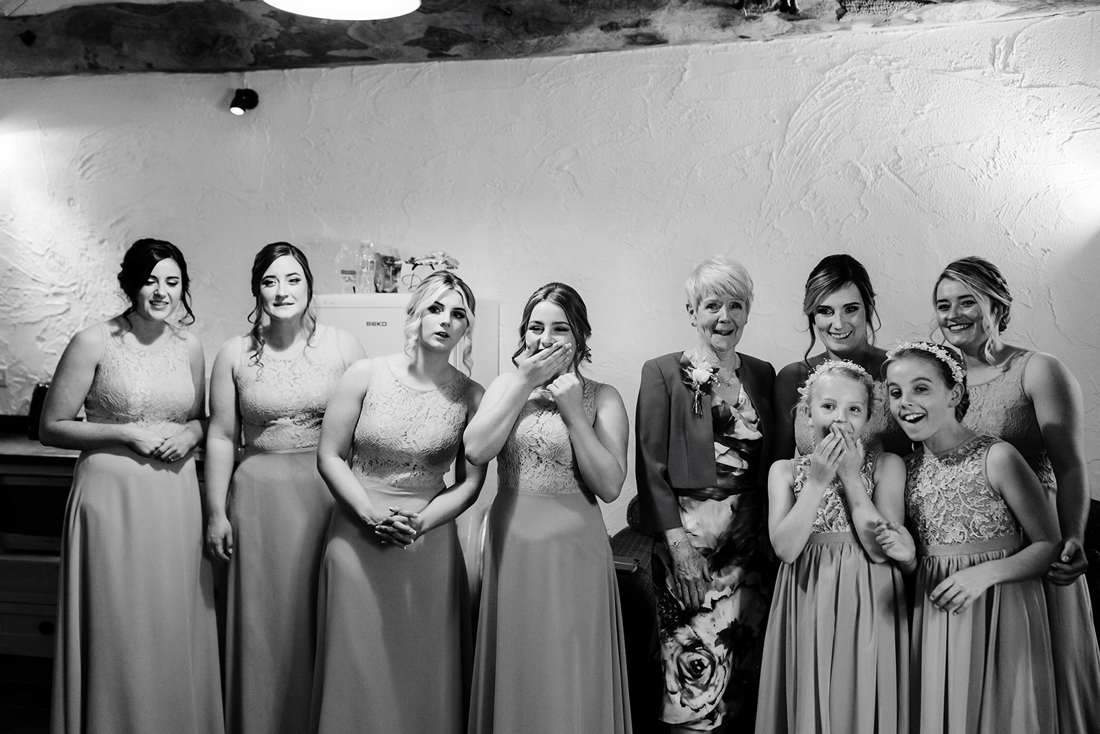 Bridesmaids and mother of the bride seeing the bride in her dress for the first time , in black and white 