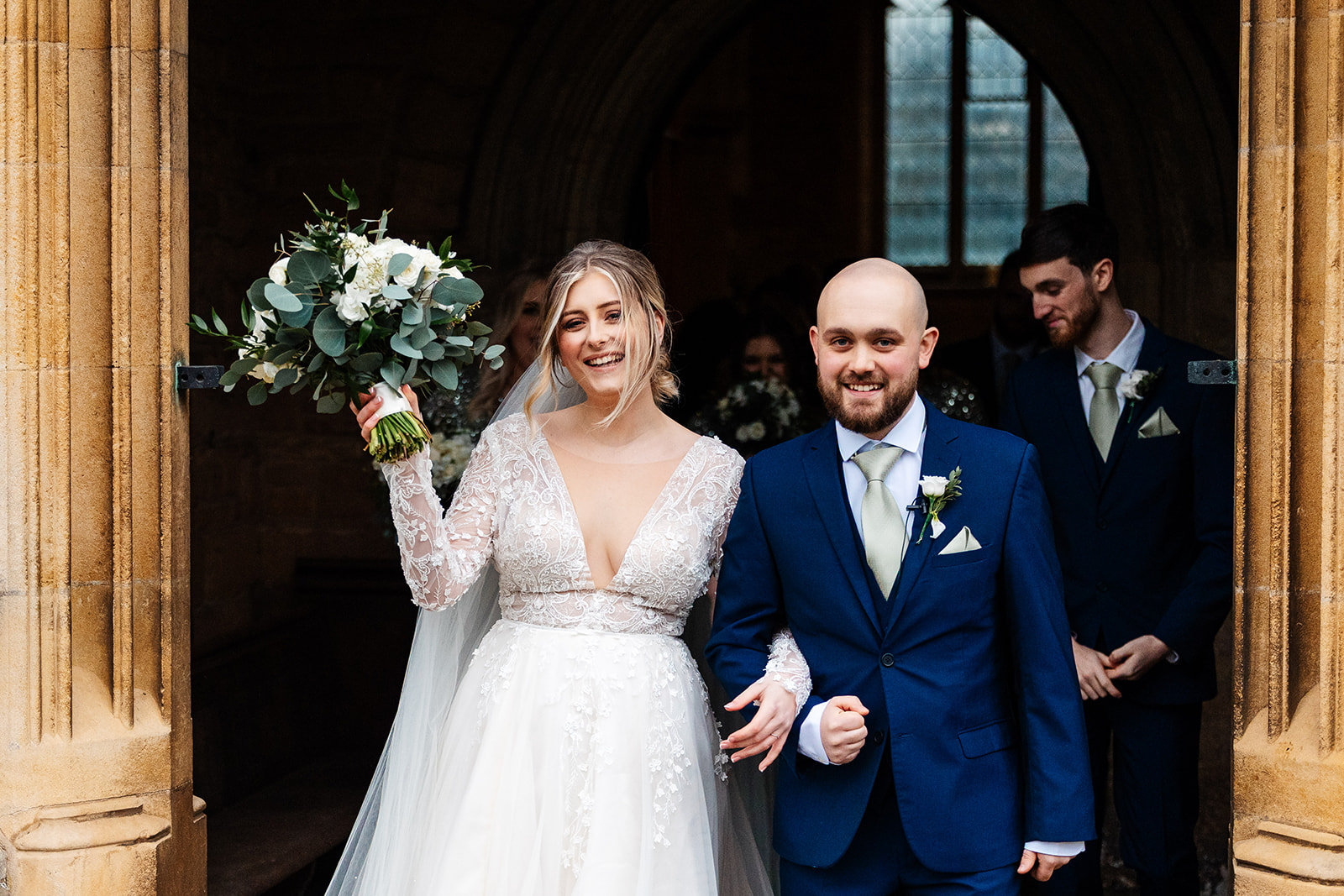 Couple leaving church after ceremony smiling, Bride holds up bouquet 