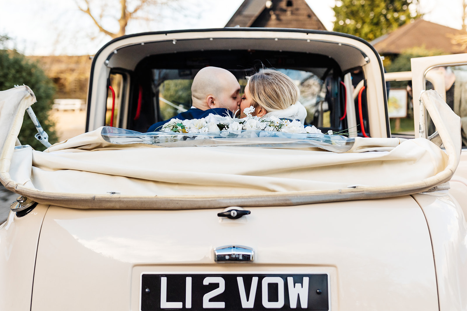 Couple leave church in vintage car with flowers in the back