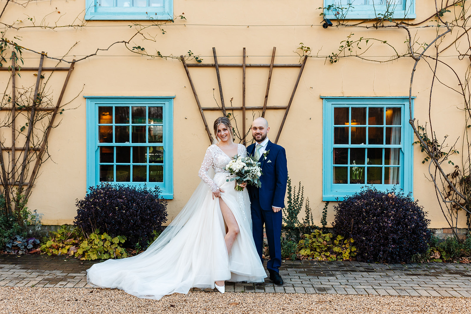 Couple infront of main house at South Farm with blue window frames and door in the background 