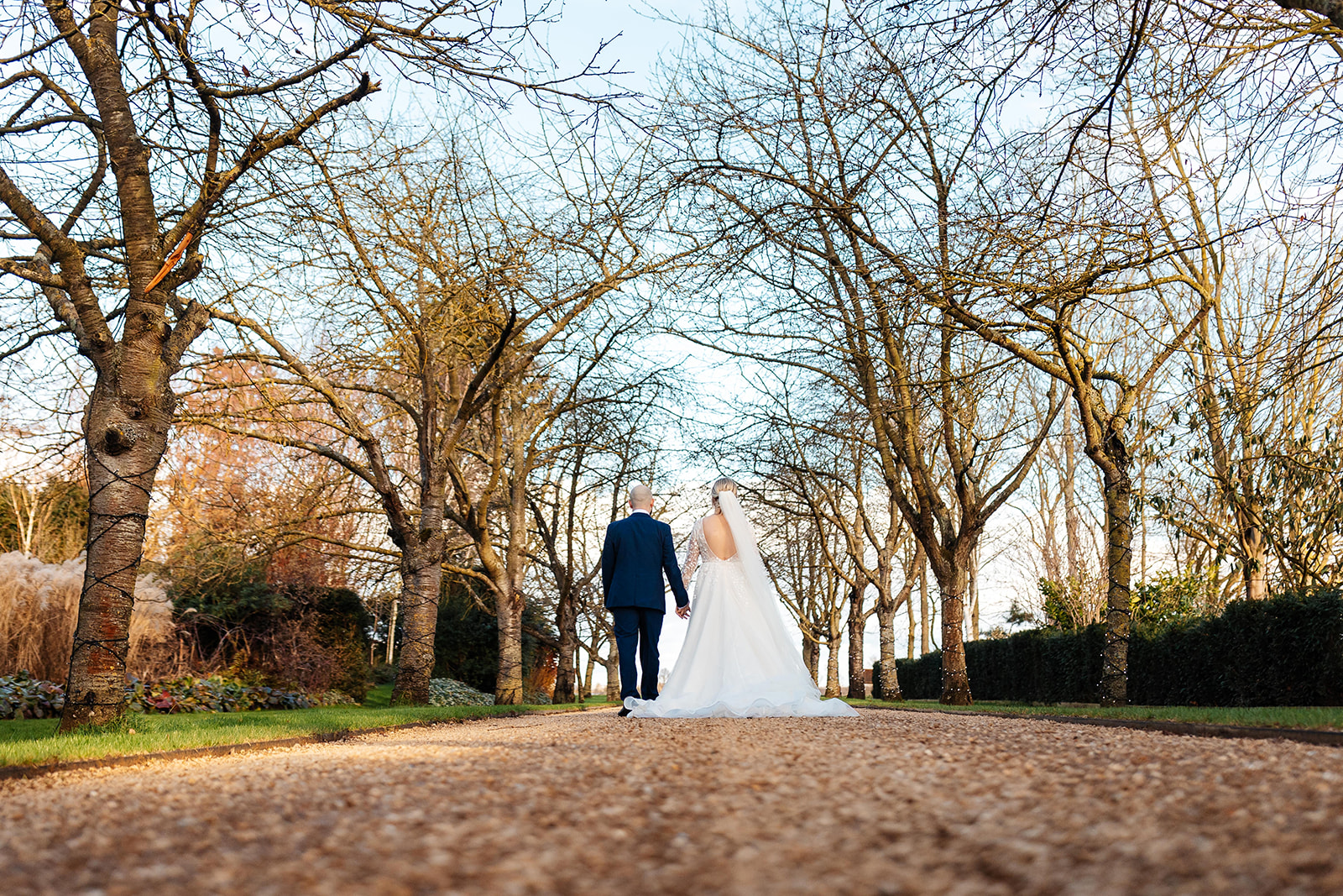 Couple walk away through tree lined walkway of South Farm holding hands 