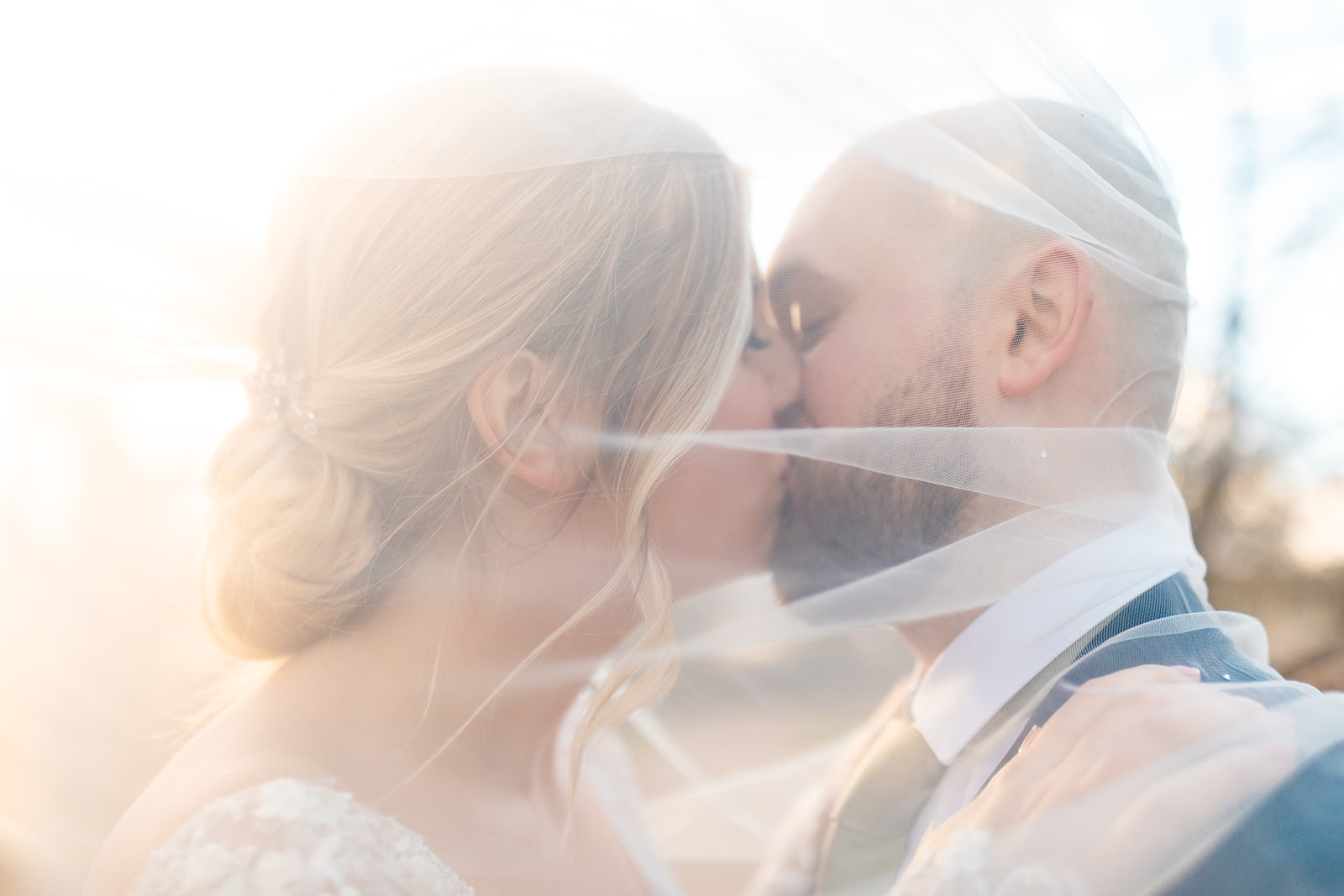 Couple kiss behind brides veil 