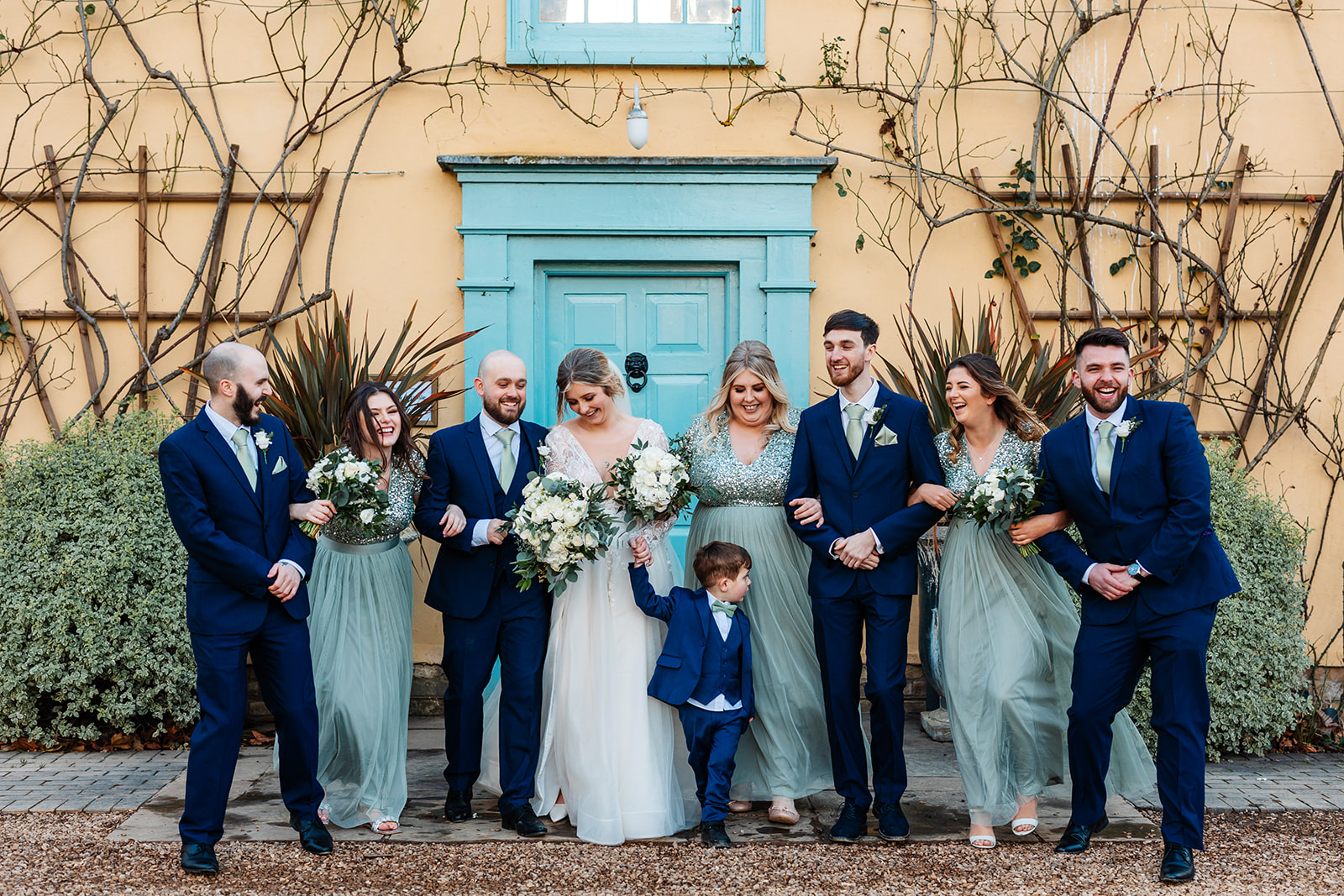 Couple with bridesmaids in green sequin dresses and groomsmen in dark blue suits outside south farm main house 