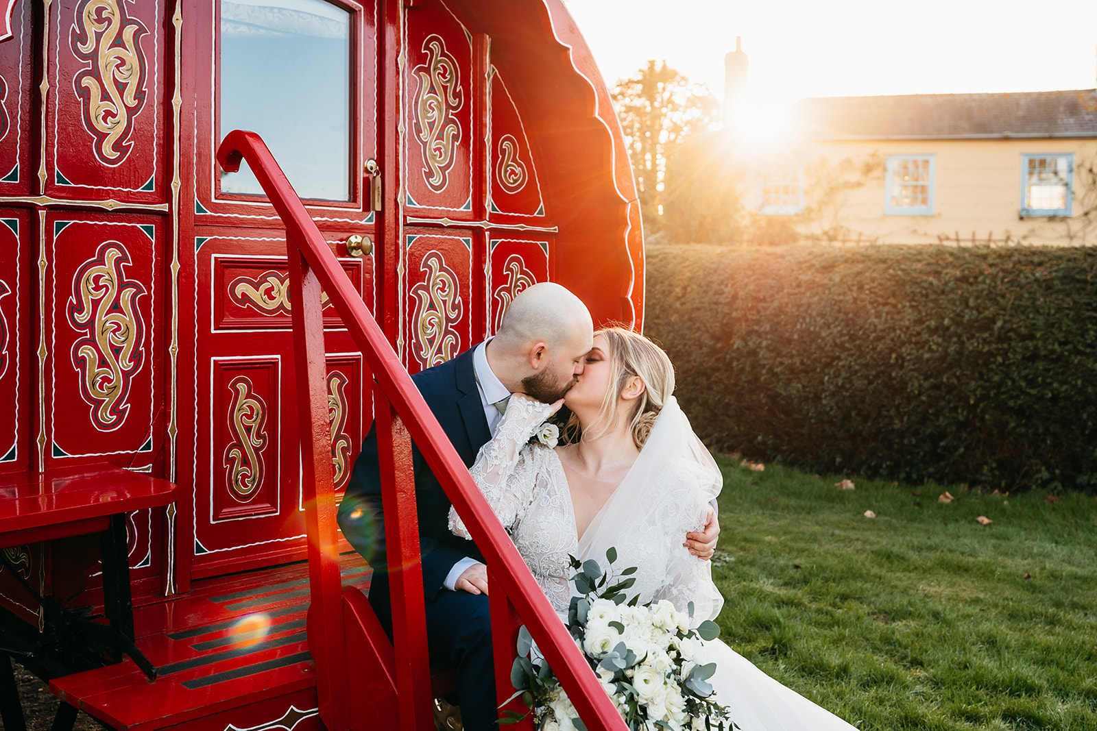 Couple share a kiss whilst sat on the steps of a traditional travelers wagon