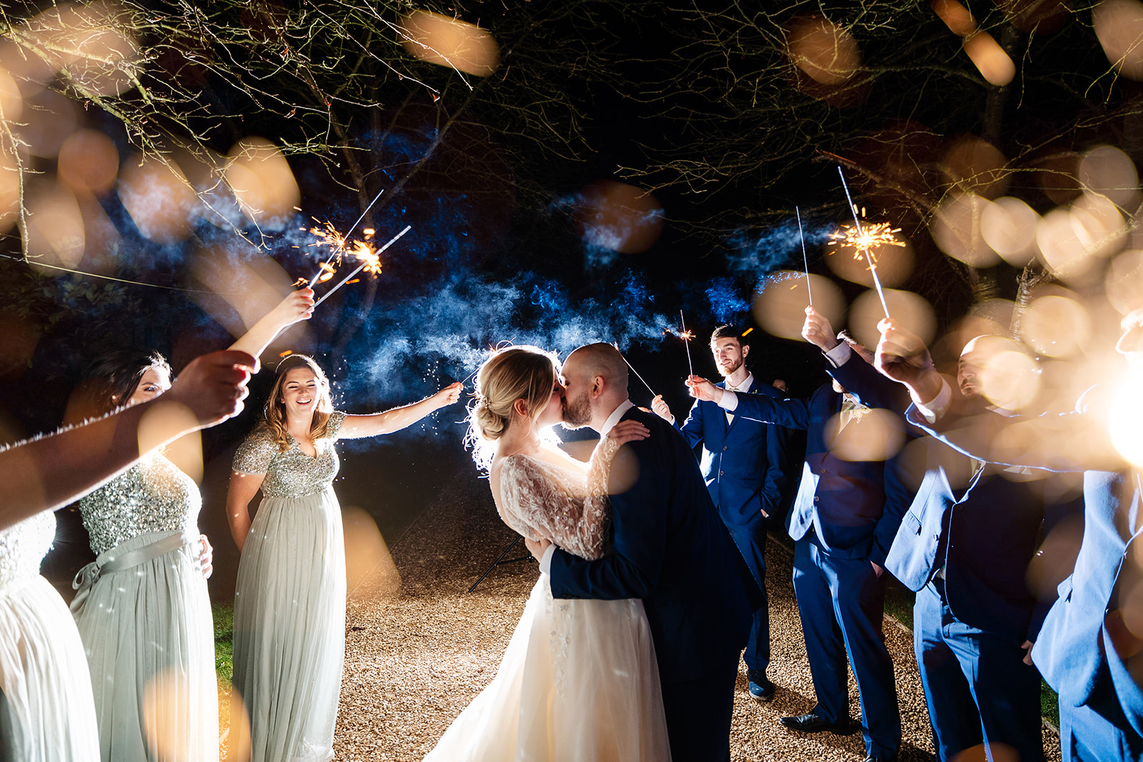Couple share a kiss in sparkler archway made by bridesmaids and groomsmen