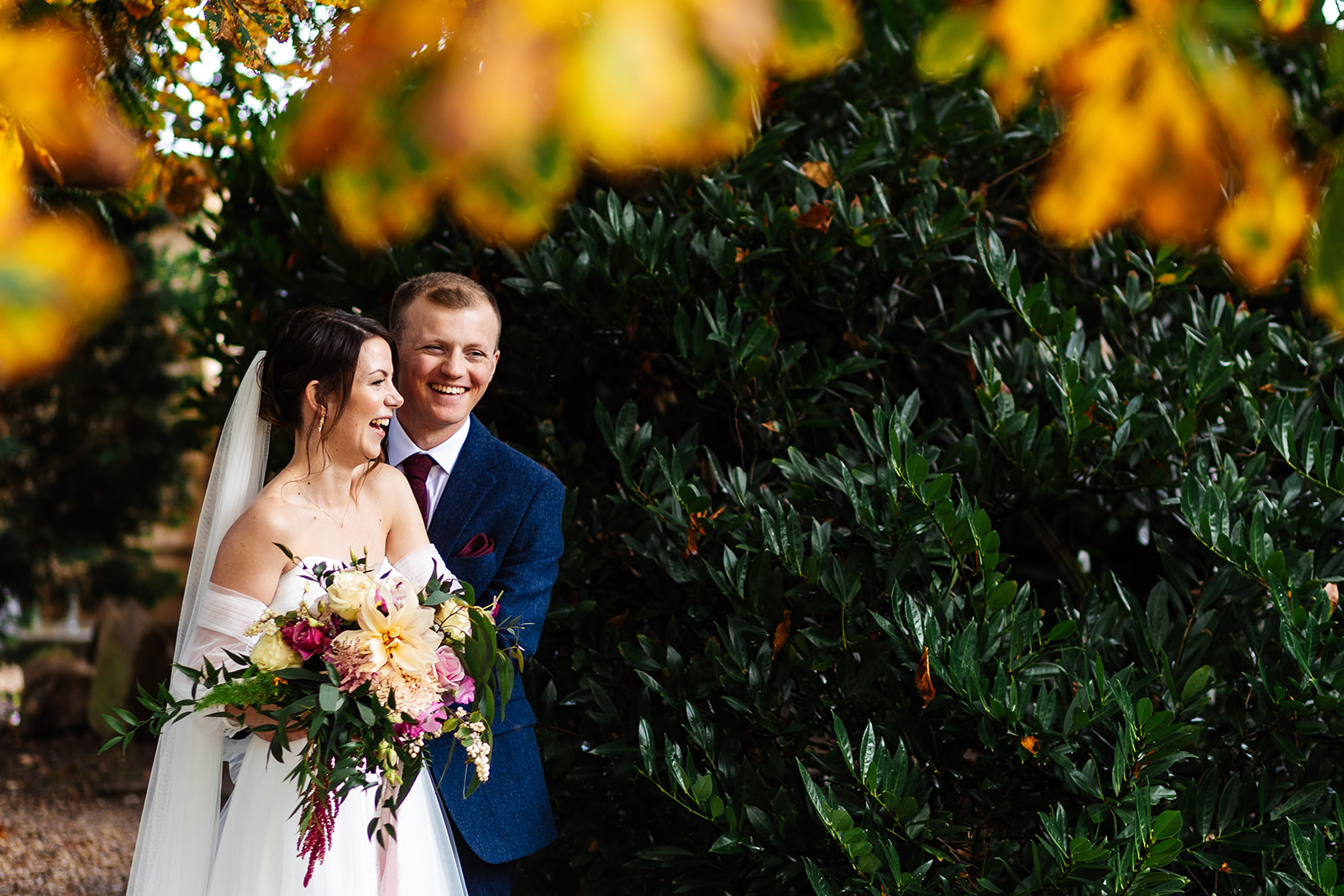 bride and groom stand together framed by green and yellow foliage at redcoats in hertfordshire