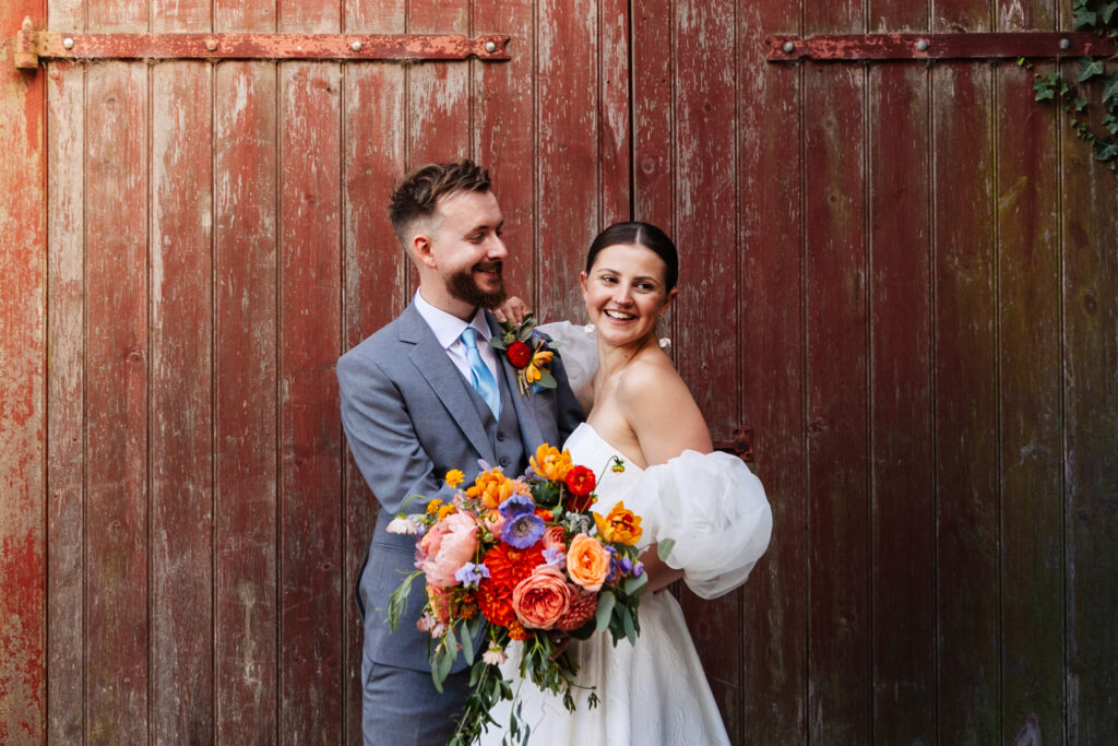 bride and groom stood in front of rustic red wooden door at south farm