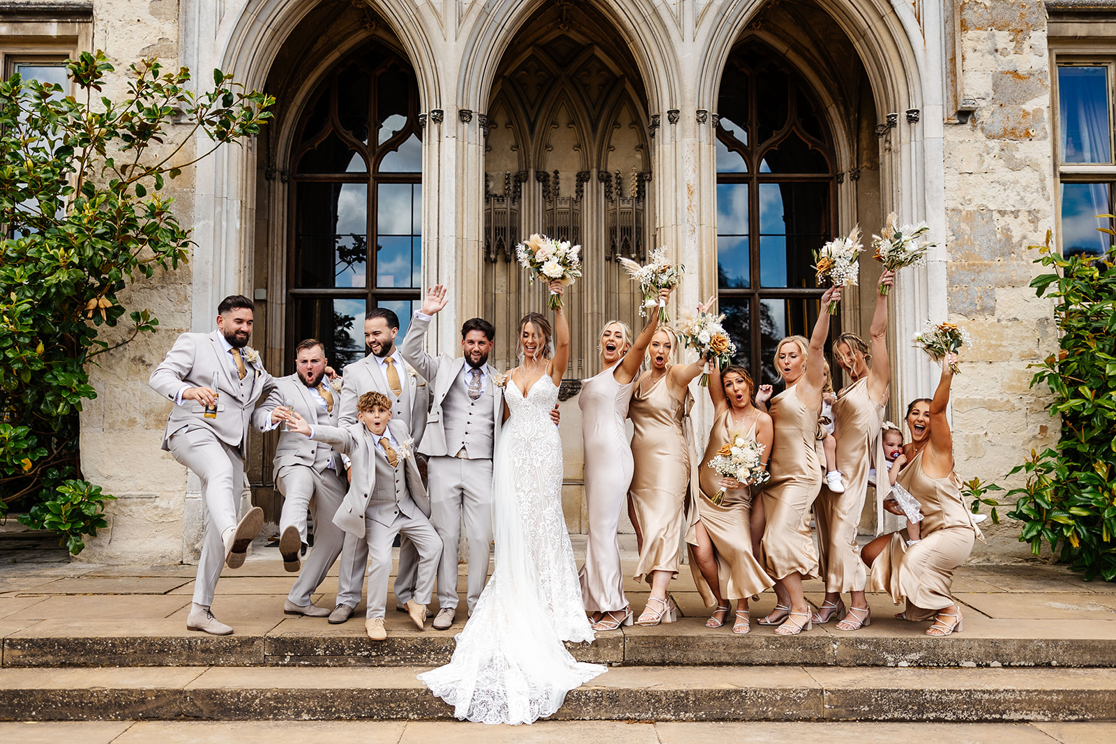 Bride & Groom on the steps of Ashridge House, groomsmen to the left and bridesmaids to the right, posing and holding up bouquets 
