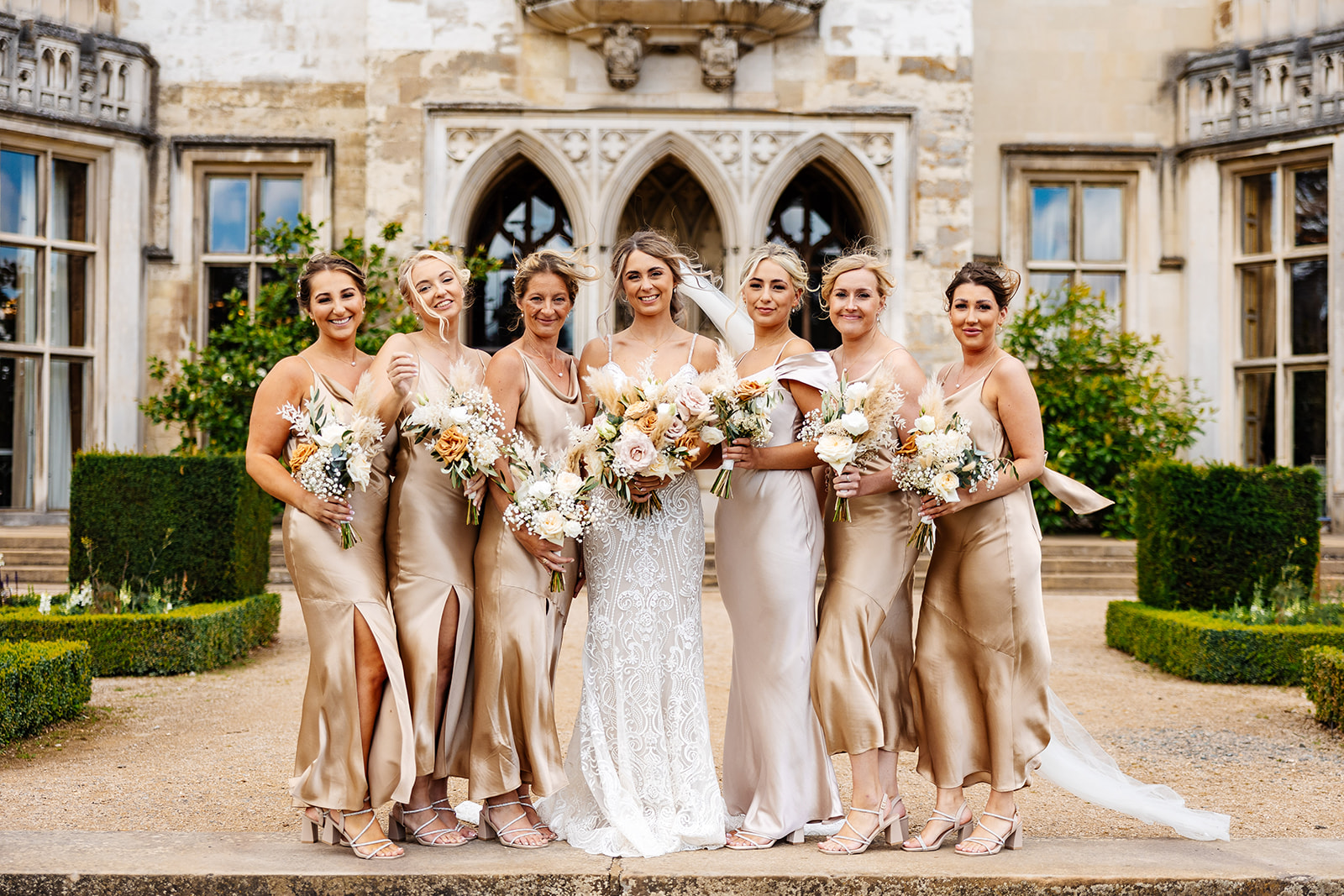 Bride with bridesmaids outside Ashridge House on the gravel pathway. All smiling and holding bouquets 