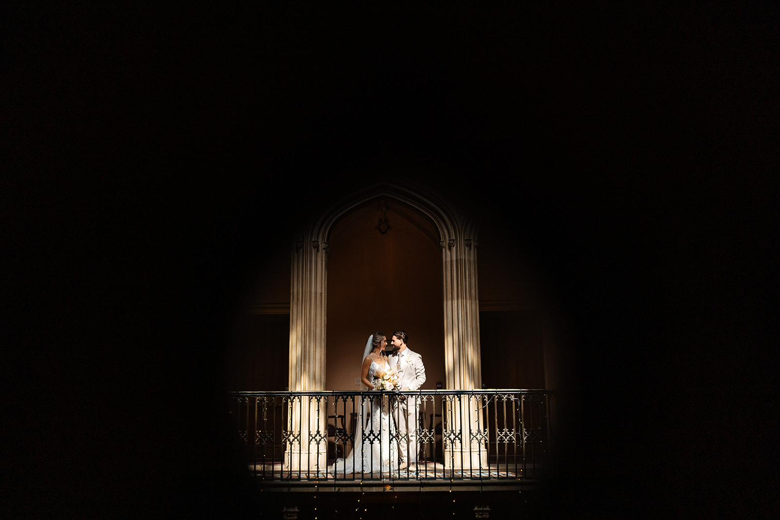 Bride and Groom on balcony inside Ashridge House, the light is hitting the stone pillars either side 