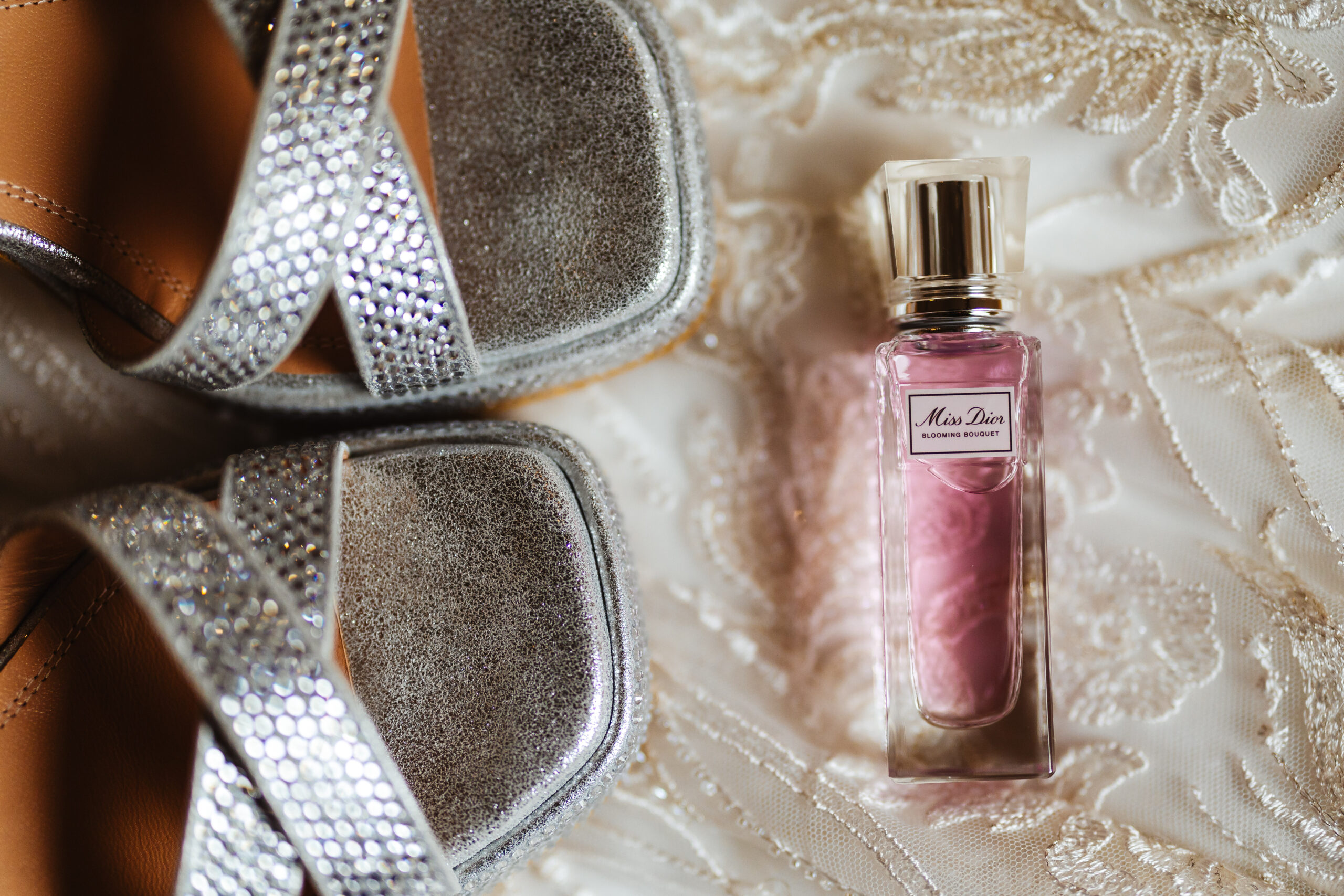 pink bottle of dior perfume and silver chunky shoes on lacy wedding dress 