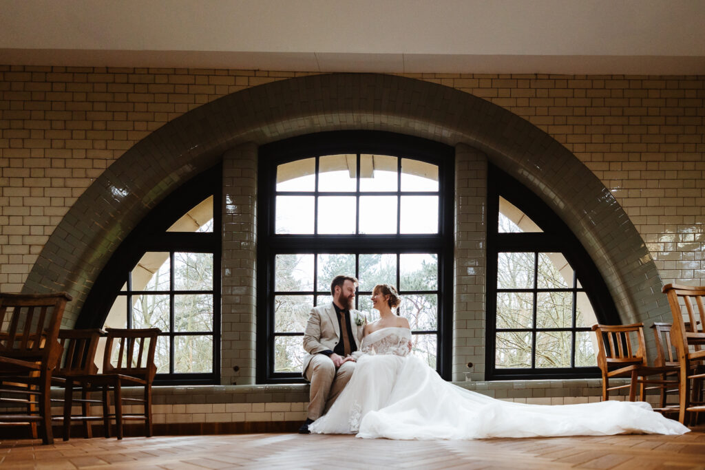 bride and groom sat on windowsill of arched window at the pumping mill