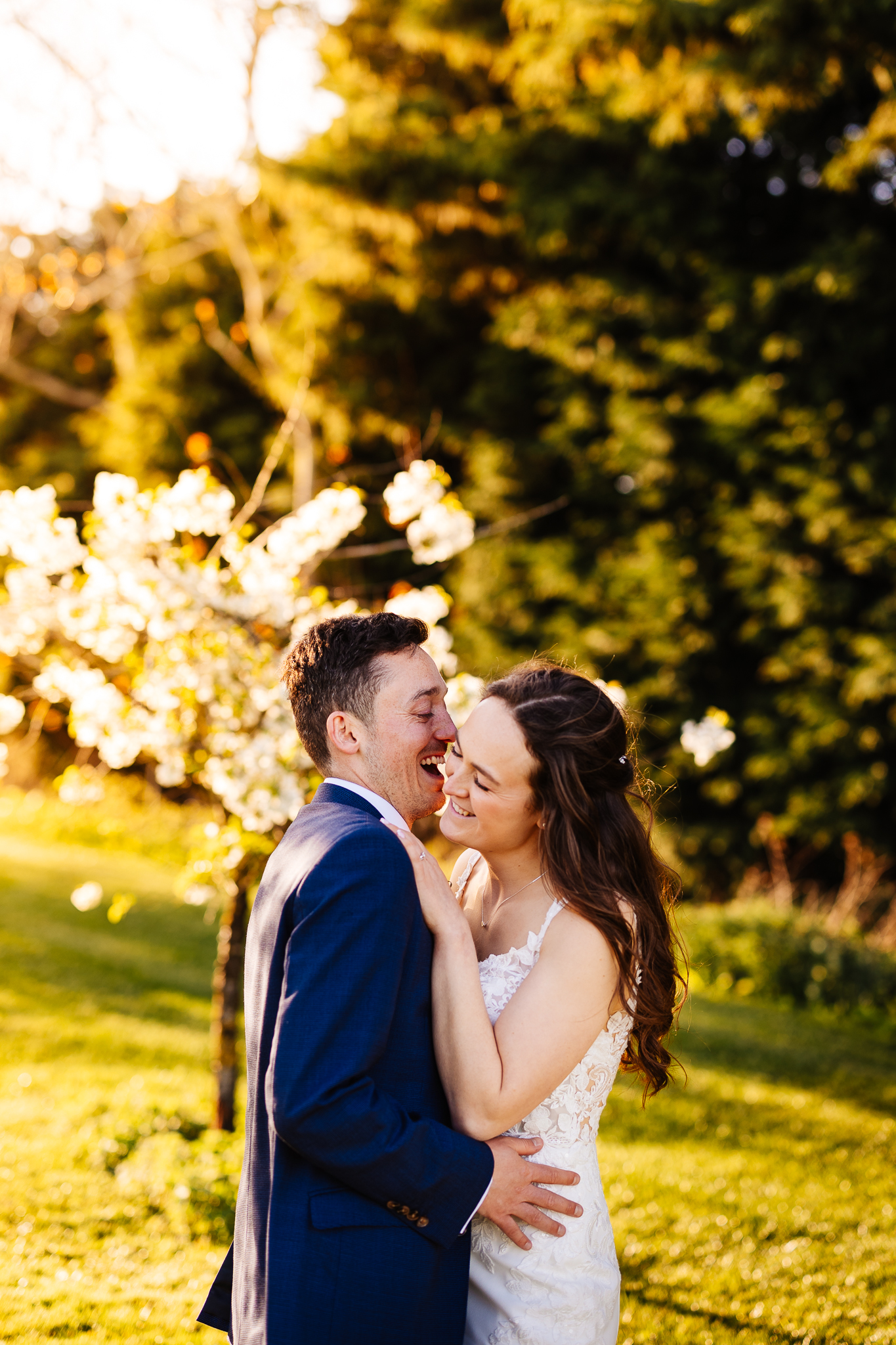 Bride and groom among pear trees laughing together. The sun is low and warm at bassmead manor barns.