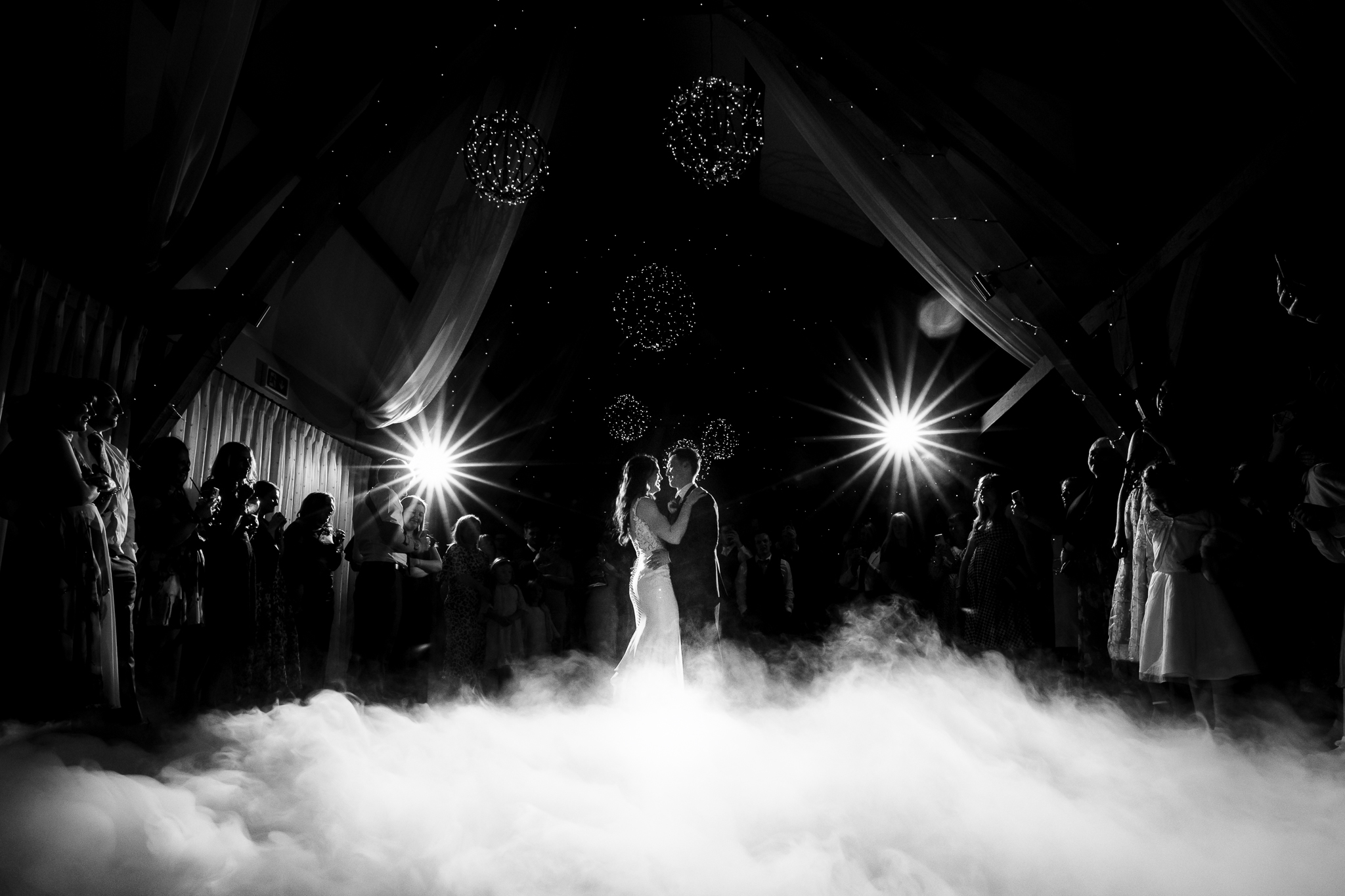 bride and groom close together dancing surrounded by friends and family at bassmead. There is a lot of fog and mist at their feet.