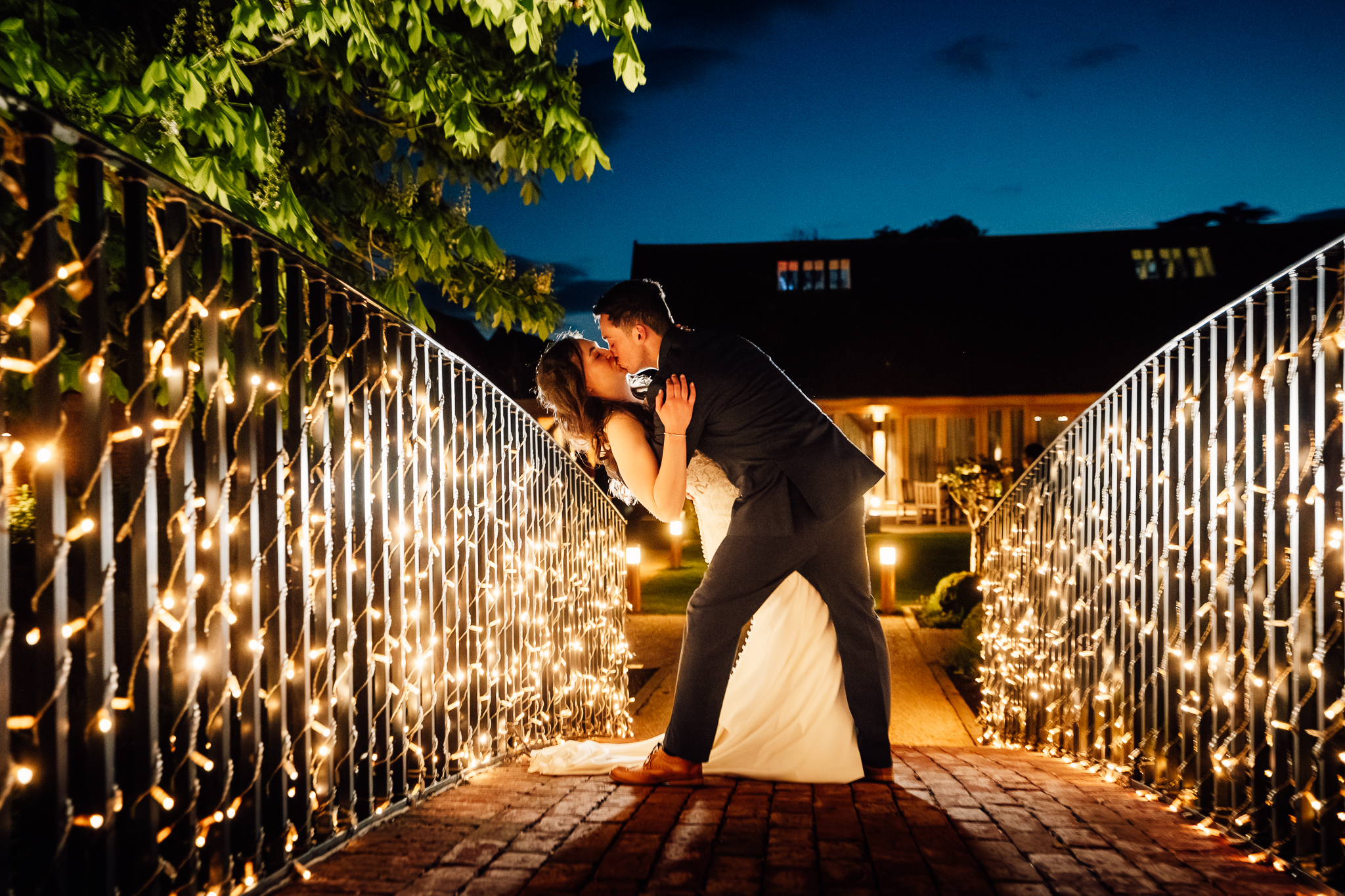 bassmead bridge shot in the evening, bride and groom leaning back for a kiss surrounded by golden lights
