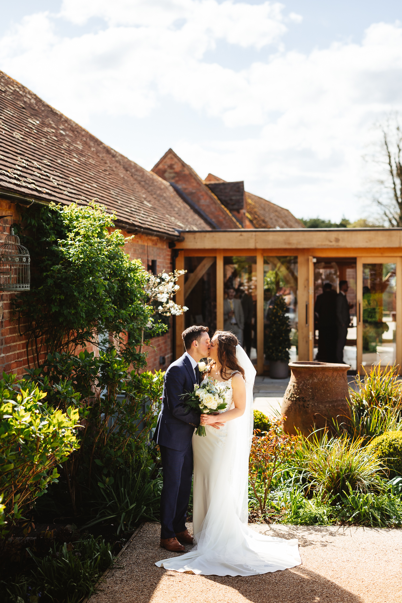 Bride and groom at bassmead surrounded by greenery, they stand together closely, kissing.
